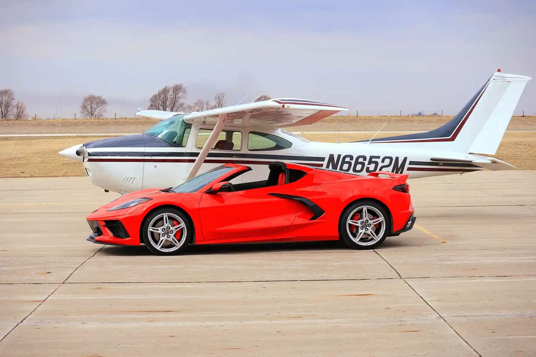 side view of a white airplane and a red sports car